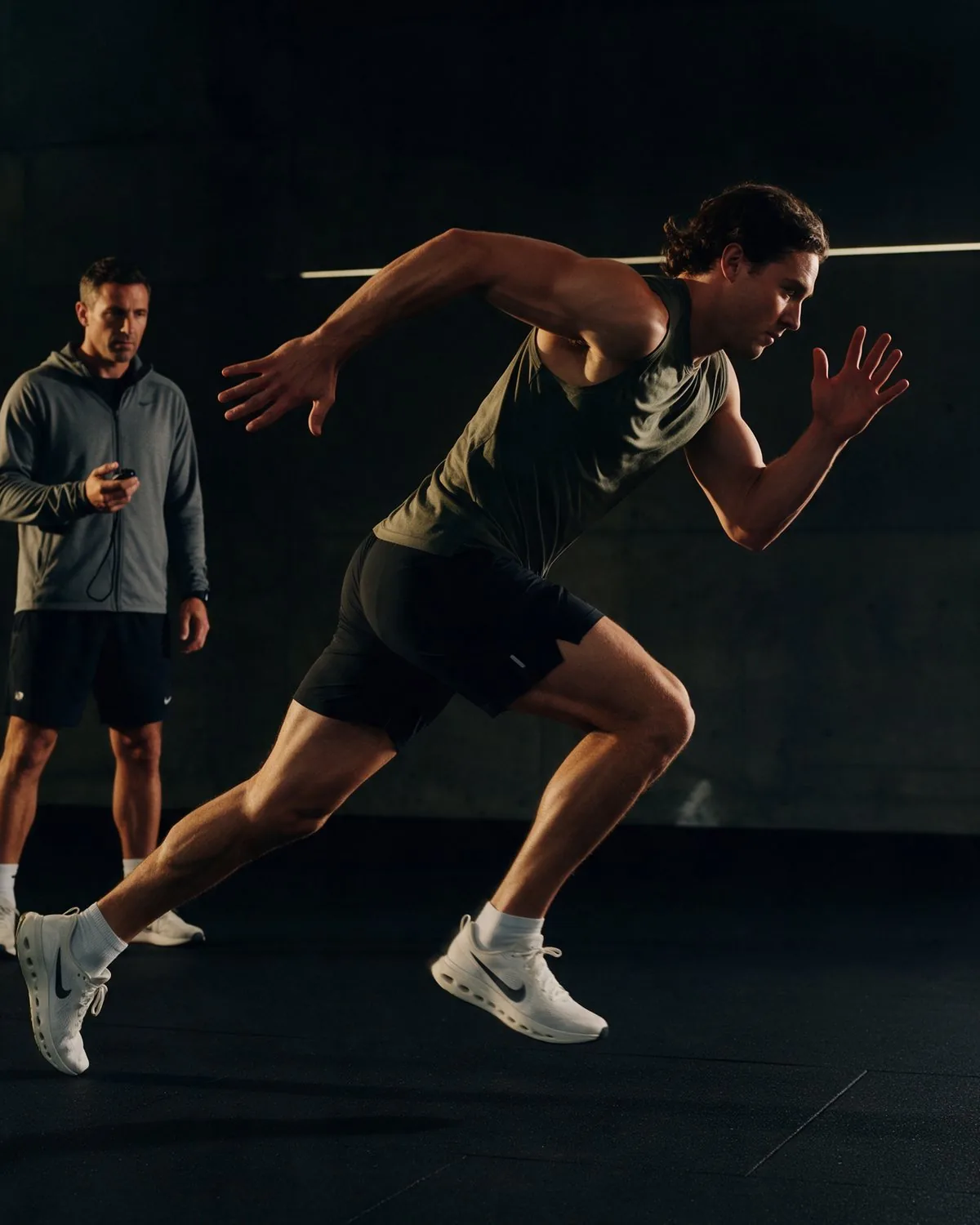 Athlet beim Sprinttraining, im Hintergrund ein Trainer